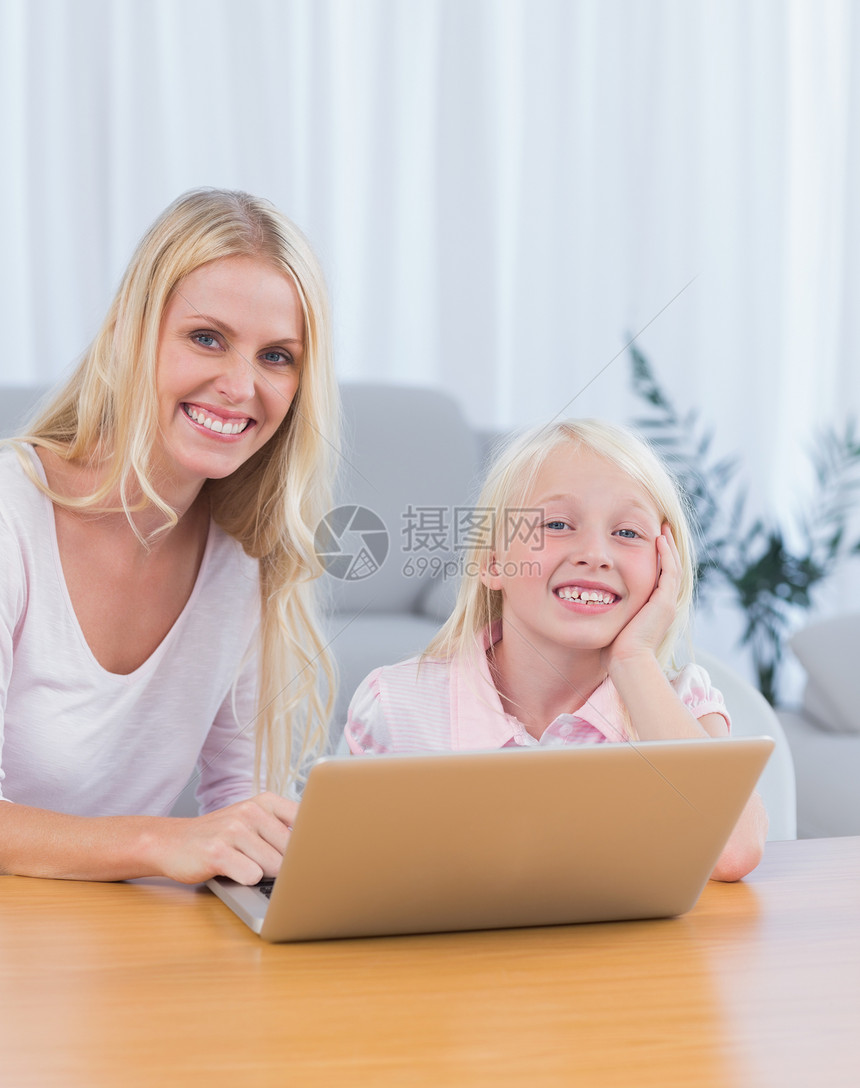 母亲和女儿在客厅使用笔记本电脑技术女孩浅色长椅金发女性孩子金发女郎微笑桌子图片