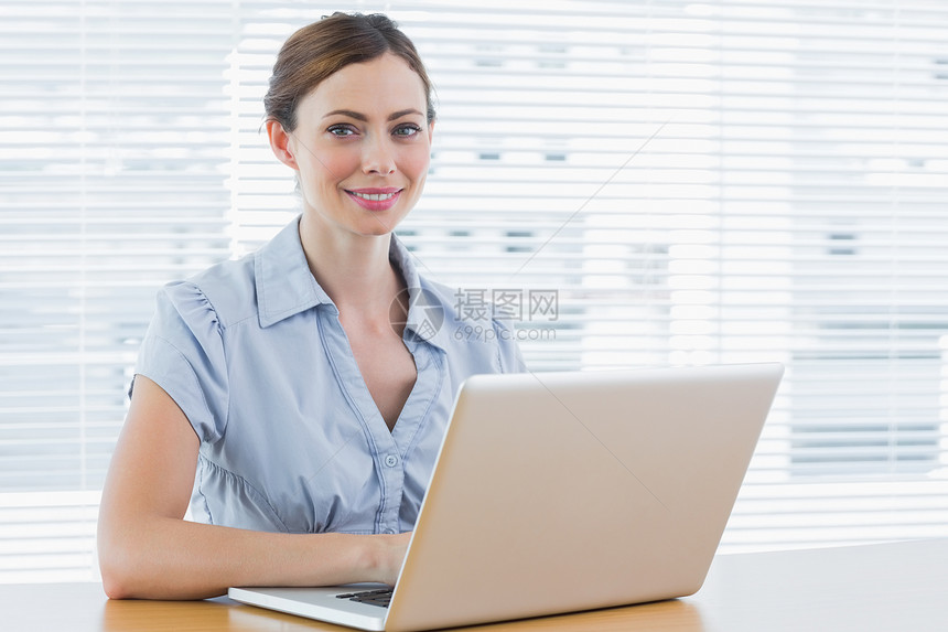 年轻女商务人士对着镜头微笑办公室笔记本人士头发公司女士棕色女性技术职业图片
