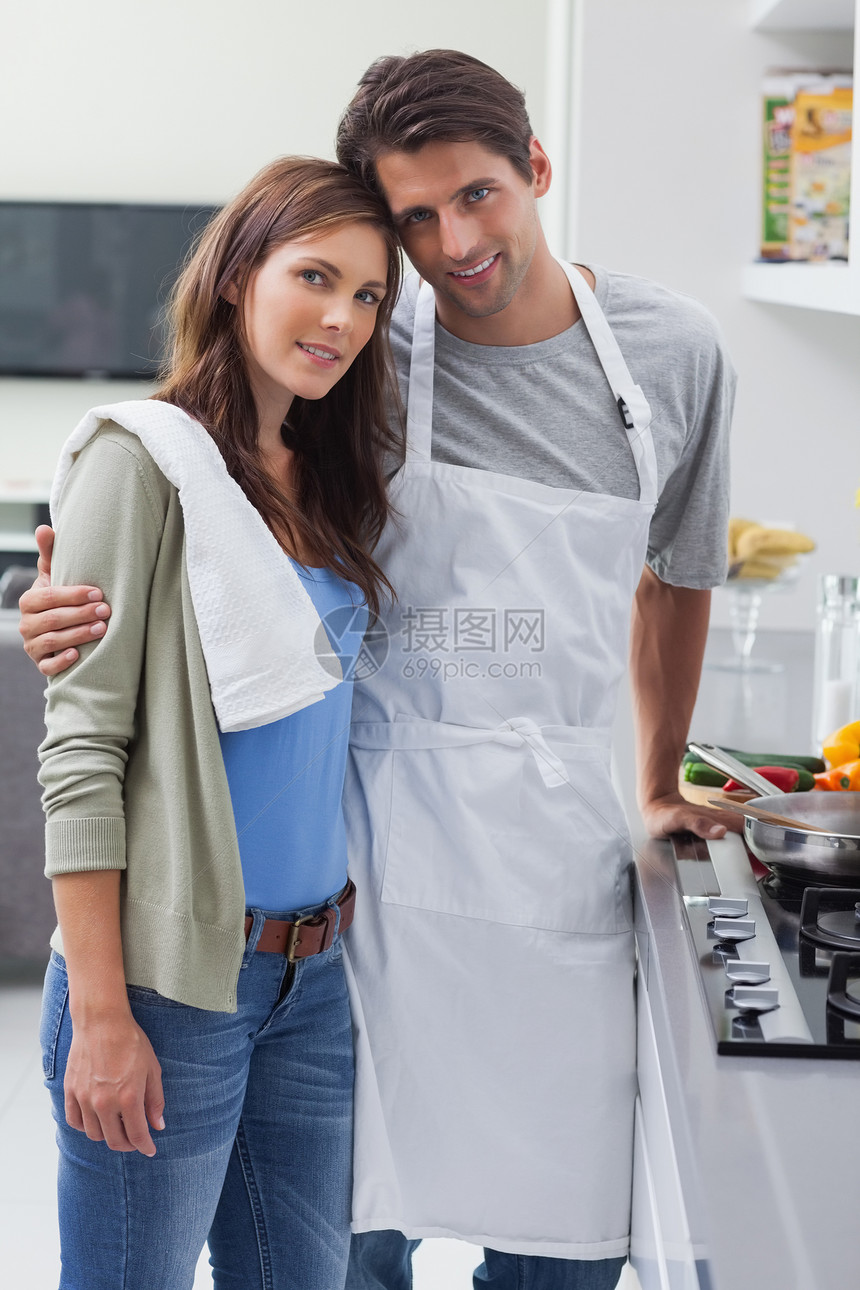 夫妻在厨房里拥抱炉顶准备男性男人微笑平底锅滚刀房子围裙台面图片