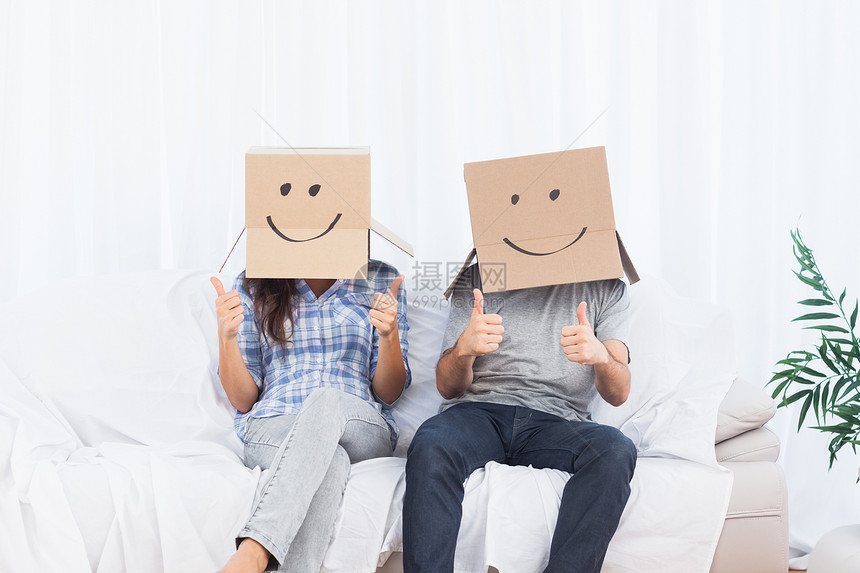 一对夫妇坐在头上戴着纸板盒的情侣举起拇指图片