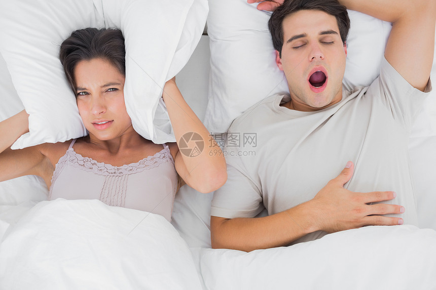 女人用垫子遮住耳朵 而她的伴侣在打呼噜图片