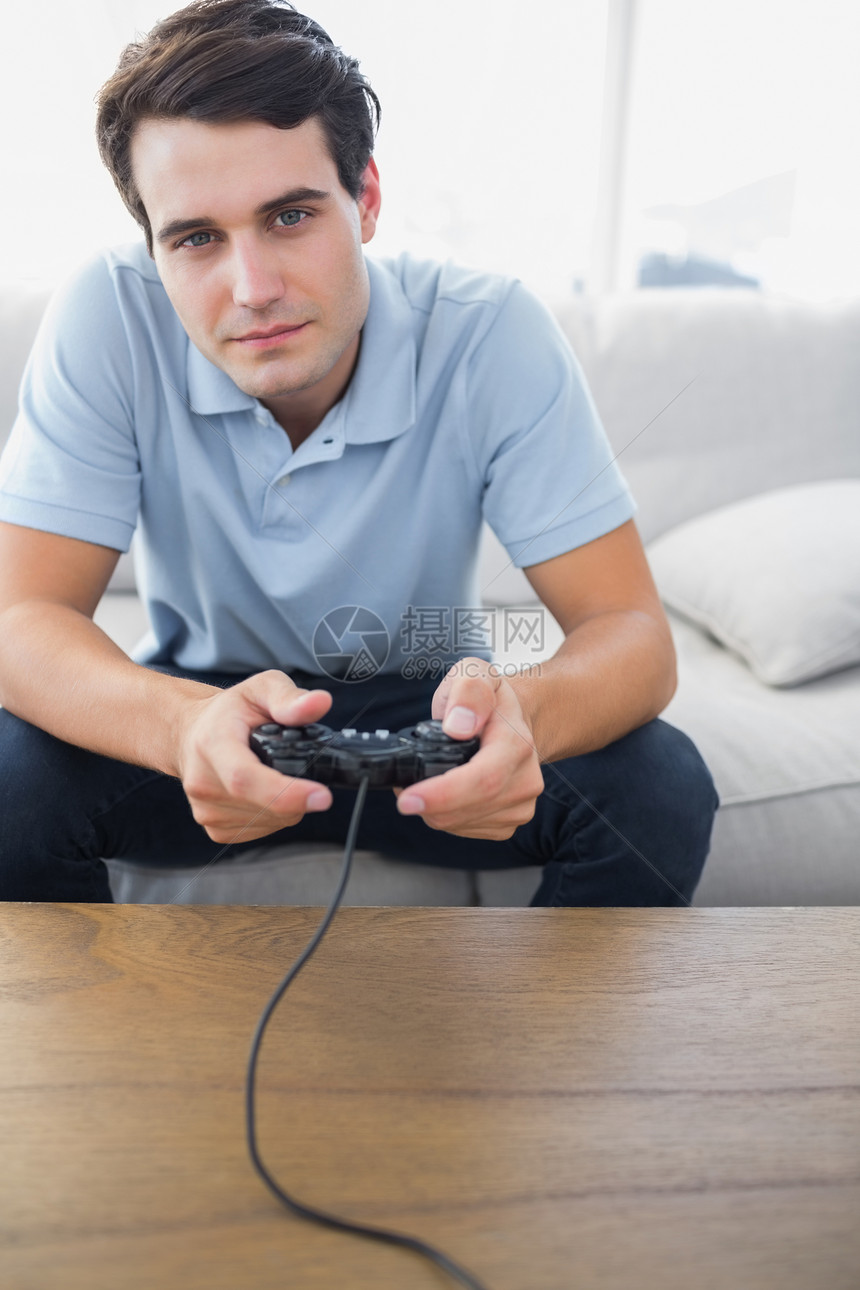 男人坐在沙发上玩电玩游戏视频游戏长椅微笑茶几家庭短发房子休息室娱乐图片