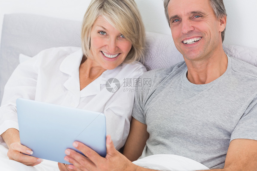 两人在床上用平板电脑对着镜头微笑图片