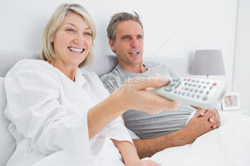 快乐的情侣在床上看电视头发睡衣金发女郎短发女性女士男性羽绒被微笑遥控图片
