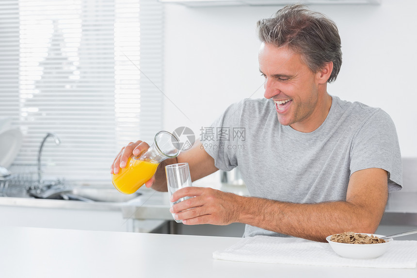 快乐的男子倒橙汁做早餐图片