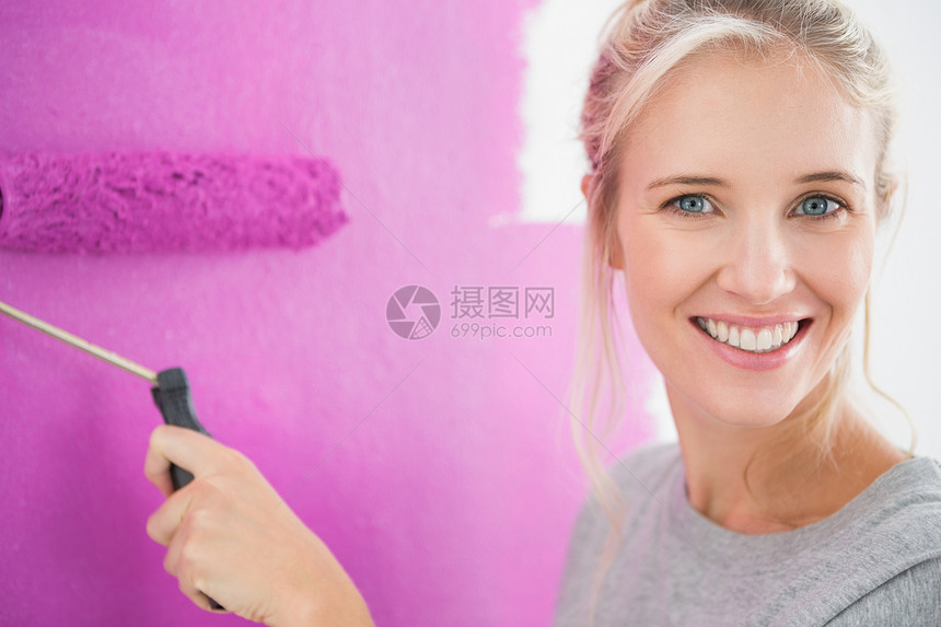 微笑的女人把墙壁涂成粉红色图片