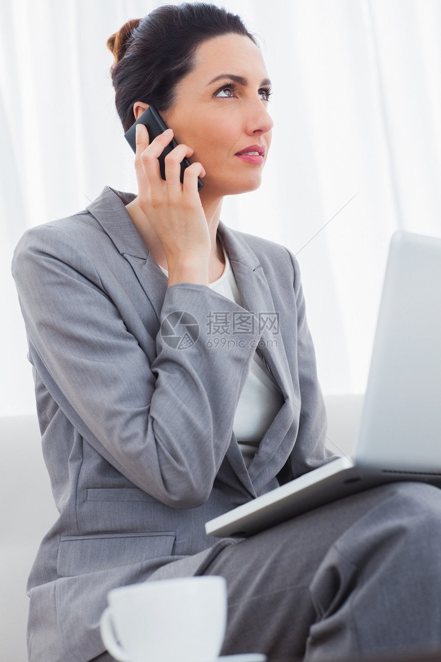 商业女商务人士用她的手机打电话 并使用笔记本电脑坐着图片