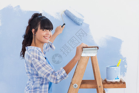 财运滚滚来妇女用涂漆滚滚来油漆墙壁 对着照相机微笑背景