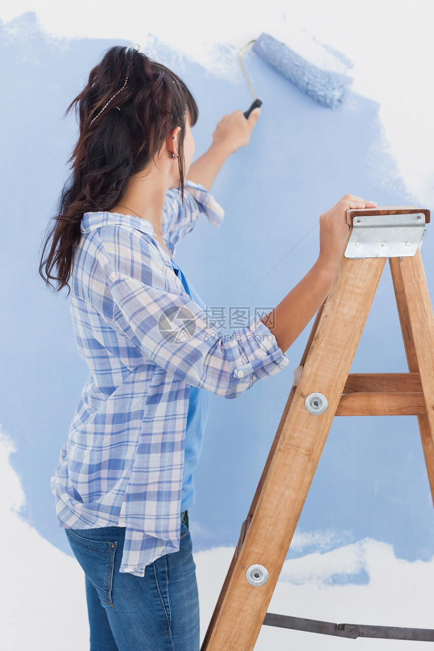 妇女用涂漆滚滚来油漆墙蓝色图片