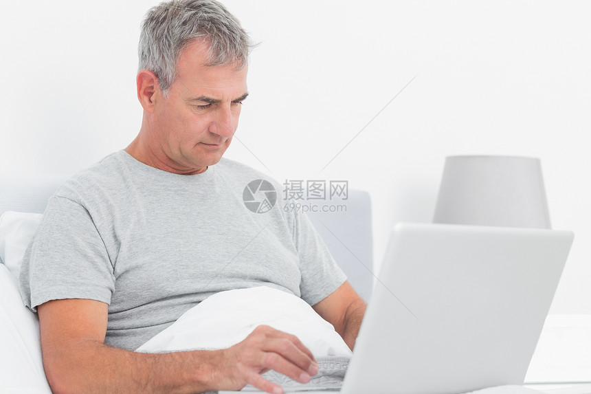 灰色头发男人在床上用笔记本电脑图片