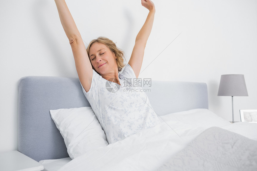 金发女人早上在床上伸展和微笑的金发女人图片