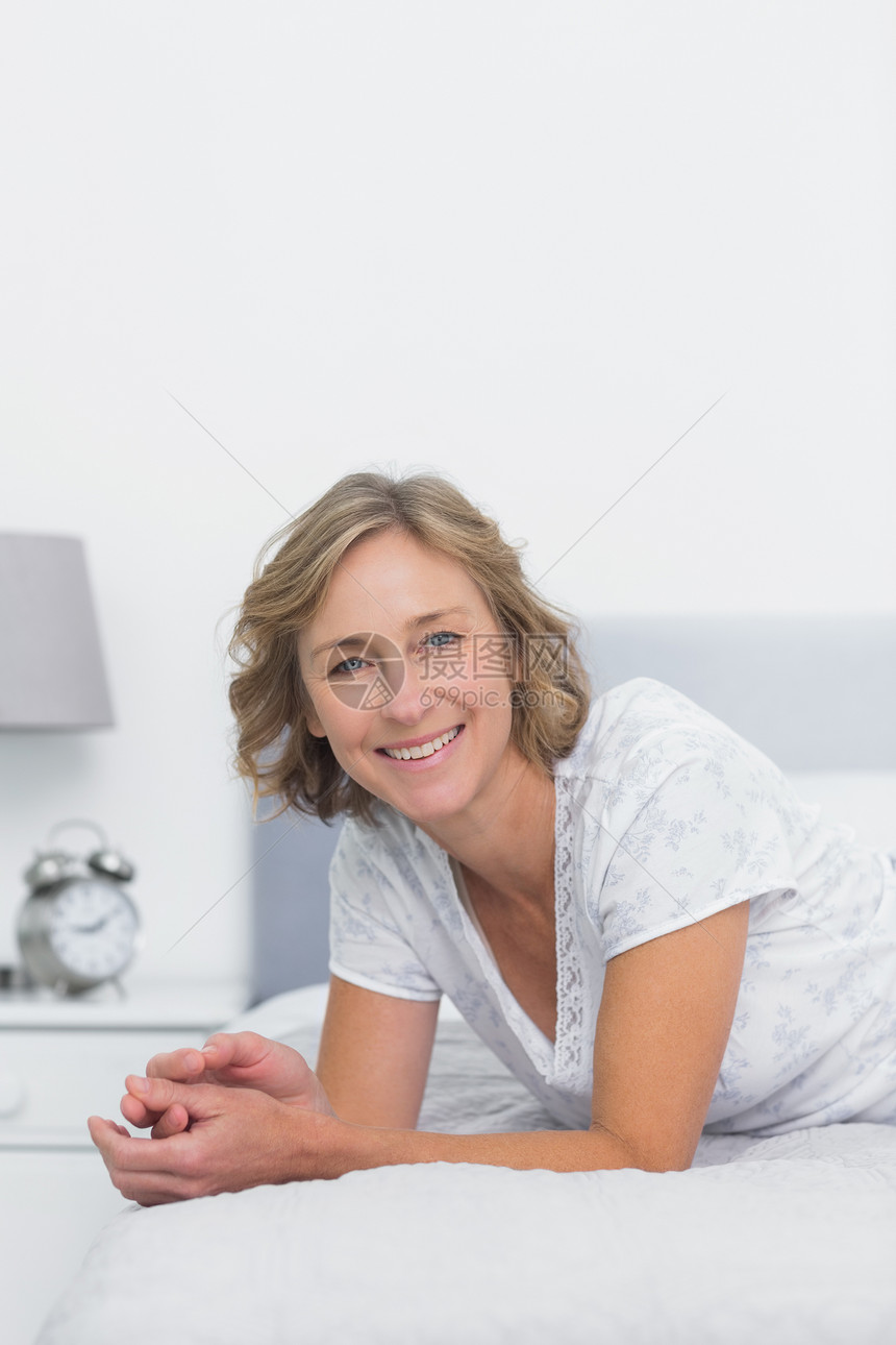 快乐的金发女人躺在床上床头柜公寓微笑短发棉被卧室浅色金发女郎睡衣女性图片
