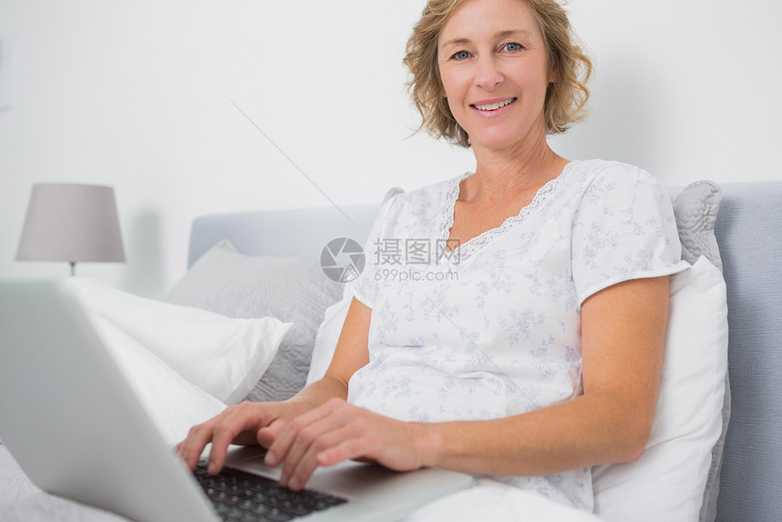 坐在床上使用笔记本电脑的金发美女图片