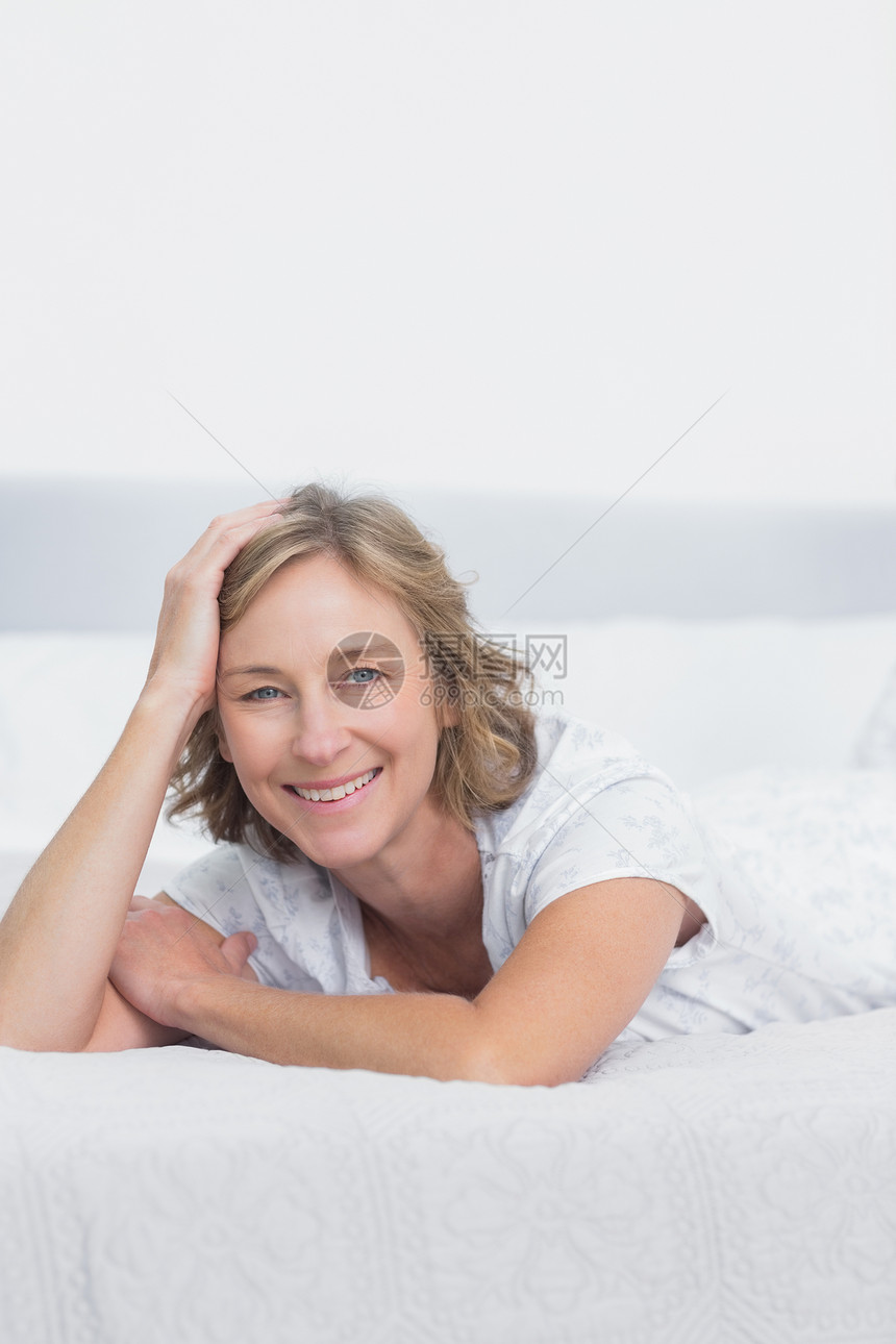 躺在床上微笑的金发女人公寓浅色枕头家庭睡衣金发女郎住所羽绒被女士女性图片