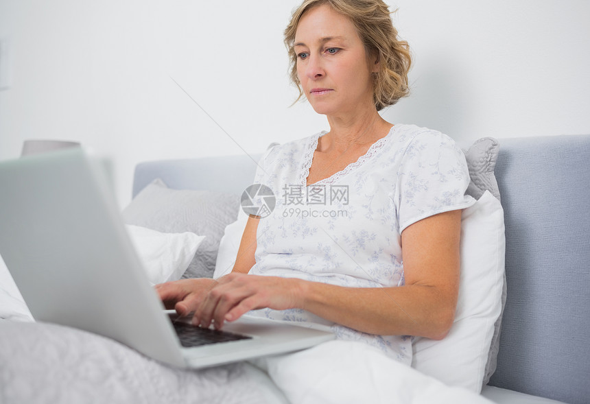 使用笔记本电脑坐在床上的金发妇女金发女郎女性公寓房子棉被坐垫卧室羽绒被枕头短发图片