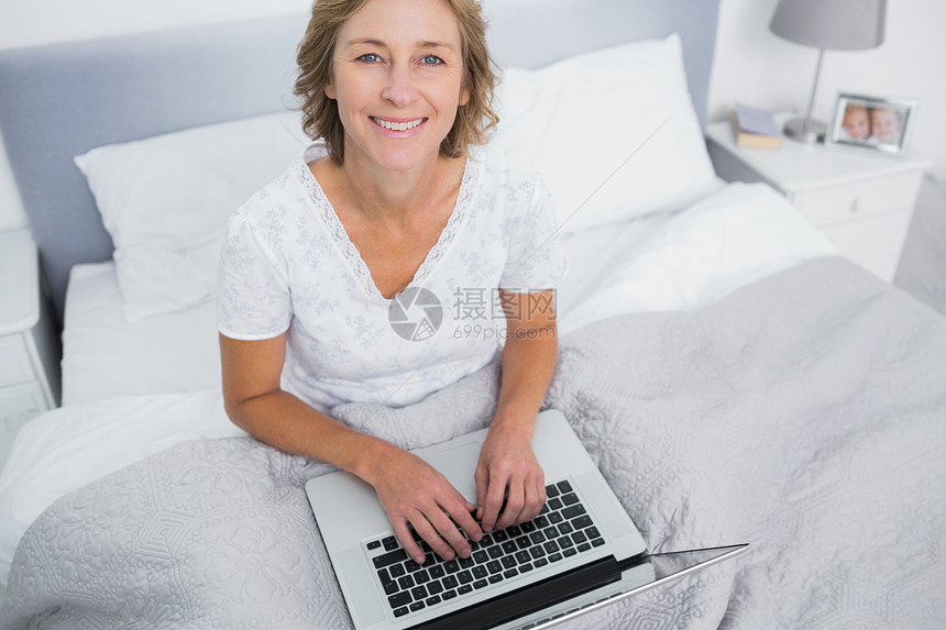利用笔记本电脑在床上微笑的金发女人图片