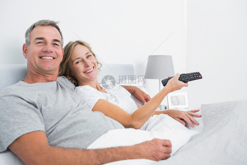 快乐的一对夫妇抱在床上看电视图片