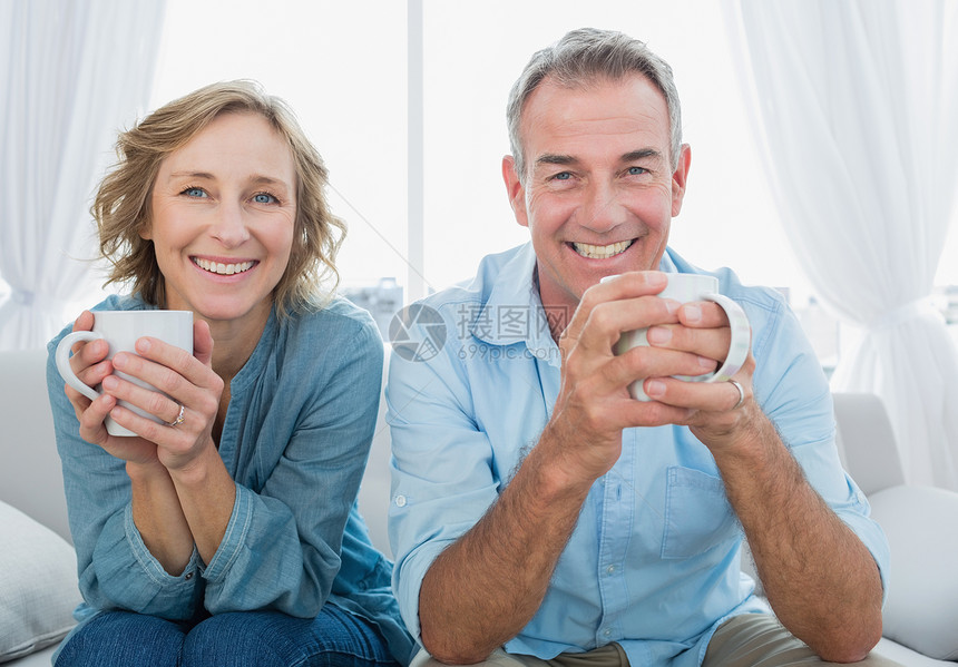 坐在沙发上喝咖啡的中年微笑的中年夫妇图片