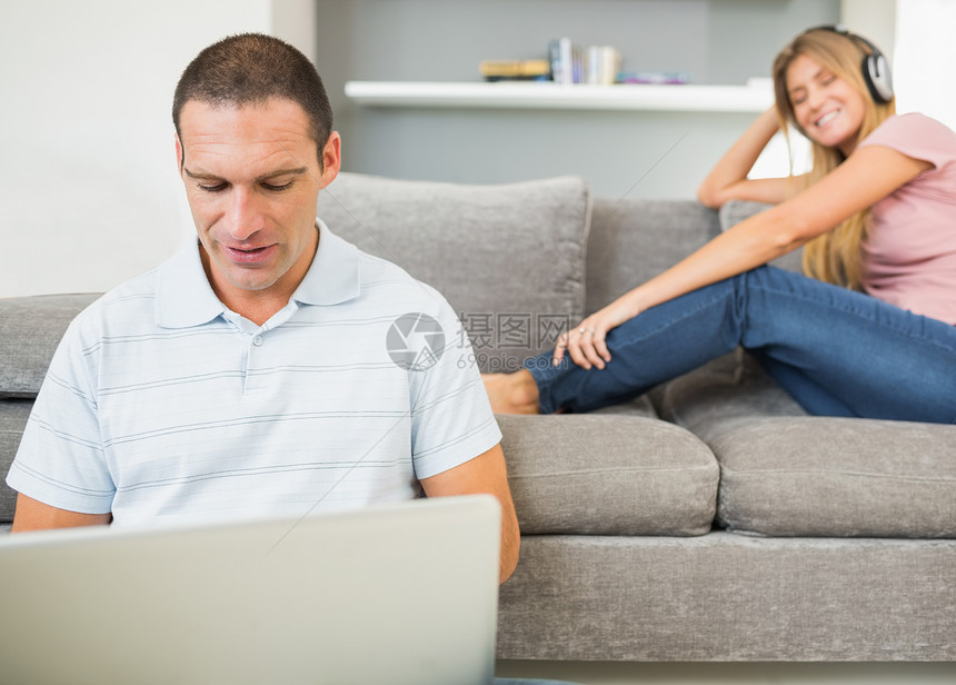 男人坐在地板上 手持笔记本电脑 女人在沙发上听音乐图片