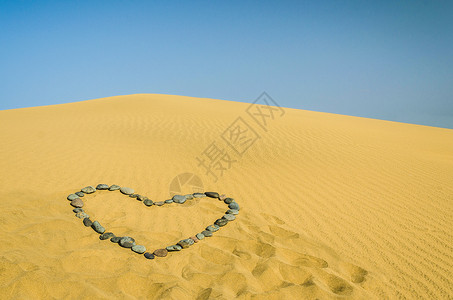 沙漠之心心在沙沙中海滩太阳沙粒天空波纹谷物爬坡蓝色心形假期背景