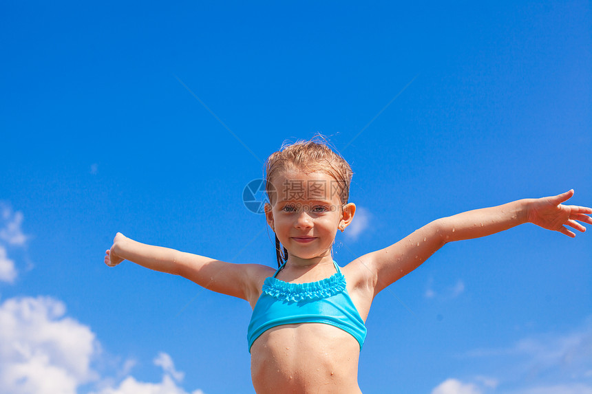 美丽的小女孩张开她的手臂背景 蓝天的蓝色天空图片