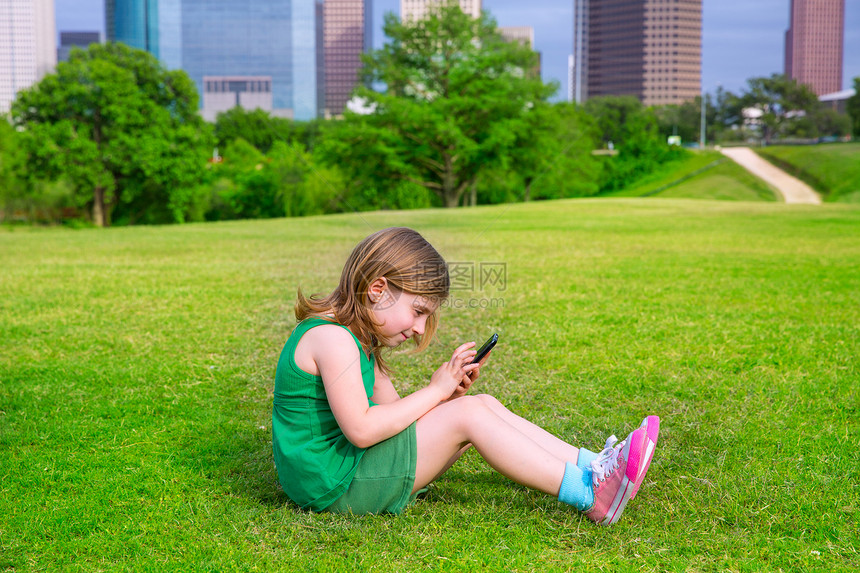 坐在C区公园草坪上玩智能手机的Blond女孩技术市中心草地公园商业办公室游戏蓝色旅行地标图片