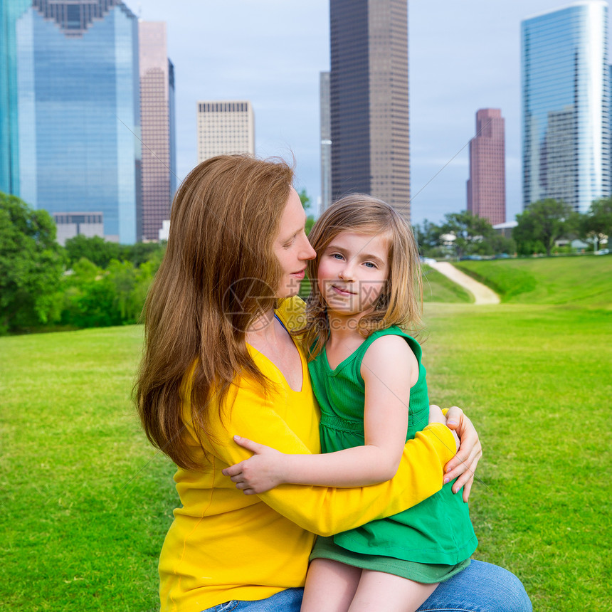 母亲和女儿在城市天际公园的快乐拥抱办公室建筑物天际地标女孩草地孩子家庭金发景观图片