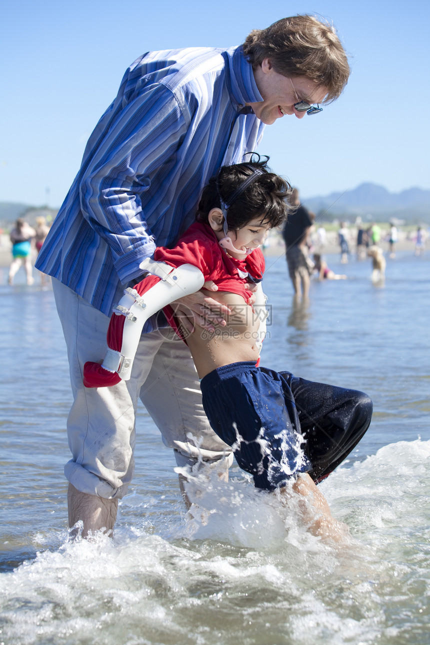 父亲帮助残疾儿子在海滩海浪中行走看门人混血儿混血需求机动性乐趣孩子男生波浪微笑图片