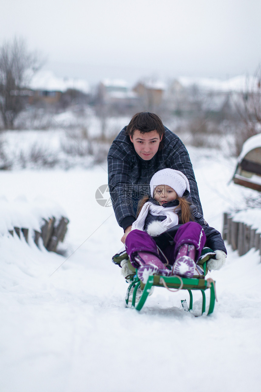 年幼的父亲和他的女儿在雪橇上骑雪橇 享受阳光明媚的冬天日闲暇家庭幸福快乐微笑女孩公园童年乐趣喜悦图片