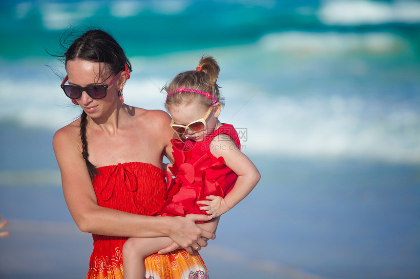 完美的年轻母亲和可爱的女儿在热带海滩上行走图片