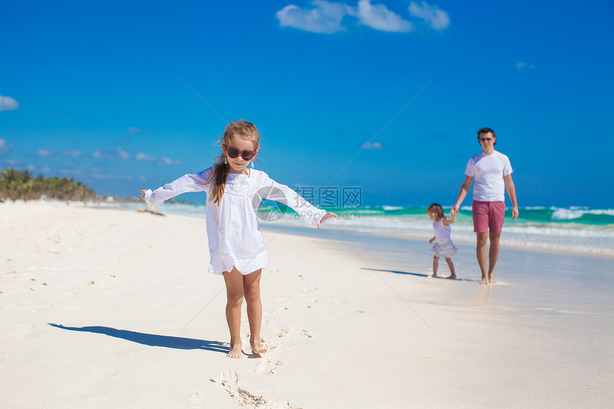 小女孩在白沙滩上和她可爱的妹妹和年轻父亲玩得开心女儿男人热带女孩海岸线享受成人海滩海岸家庭图片