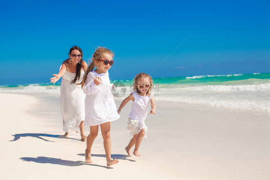 年轻快乐的母亲和可爱的女儿们 在阳光明媚的天气在异国海滩玩得开心海岸线裙子女士享受帽子热带情调海岸孩子微笑图片