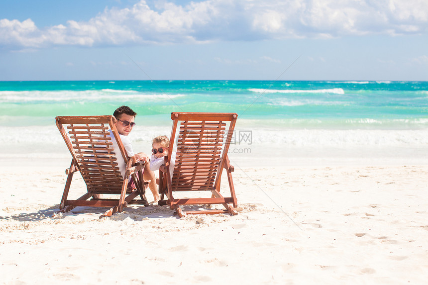 小女儿和她的年轻父亲 坐在海滩的木椅子上 看着摄像机 看着镜头图片