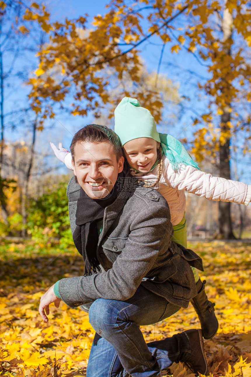 有快乐父亲的可爱小女孩 在阳光明媚的一天在秋天公园玩得开心拥抱女儿微笑叶子父母爸爸幸福成人家庭生活图片