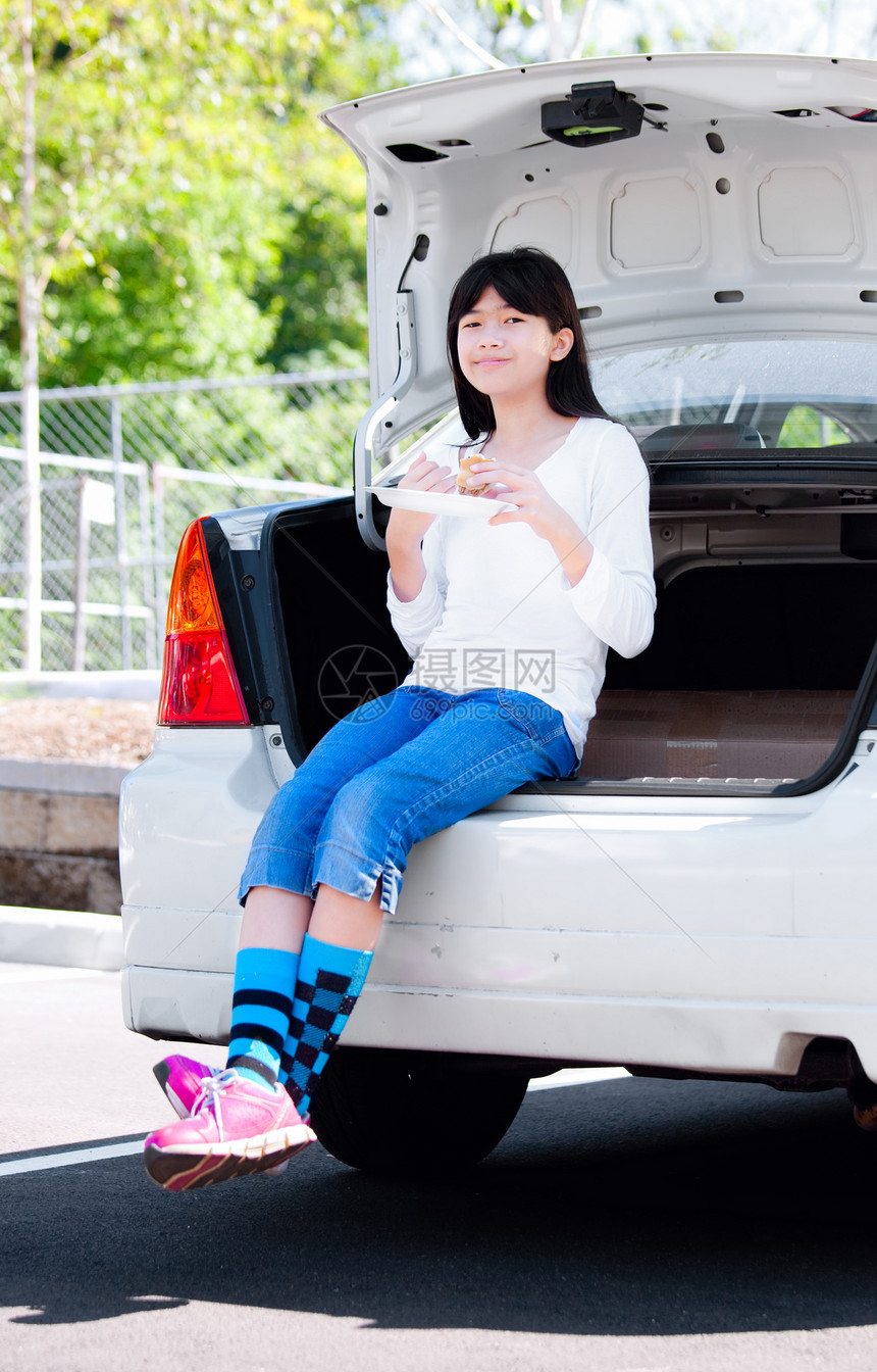 坐在后面的汽车保险杠上吃午饭的少女图片