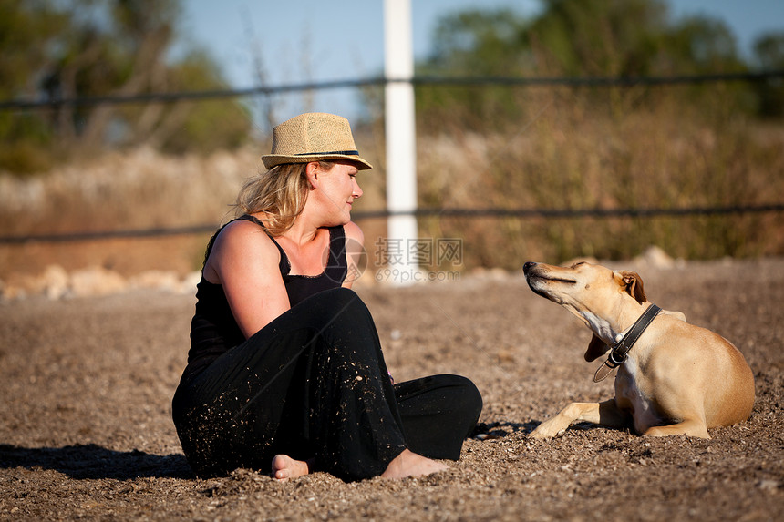 带着她的狗坐在户外的金发微笑的金发女子朋友农村乐趣女士喜悦成人场地晴天动物朋友们图片
