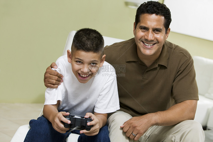 父亲和儿子在沙发上玩视频游戏 在客厅肖像中图片