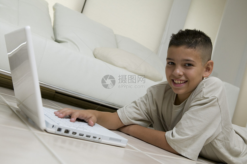 在家里客厅的地板上使用笔记本电脑对一个小快乐男孩的肖像图片