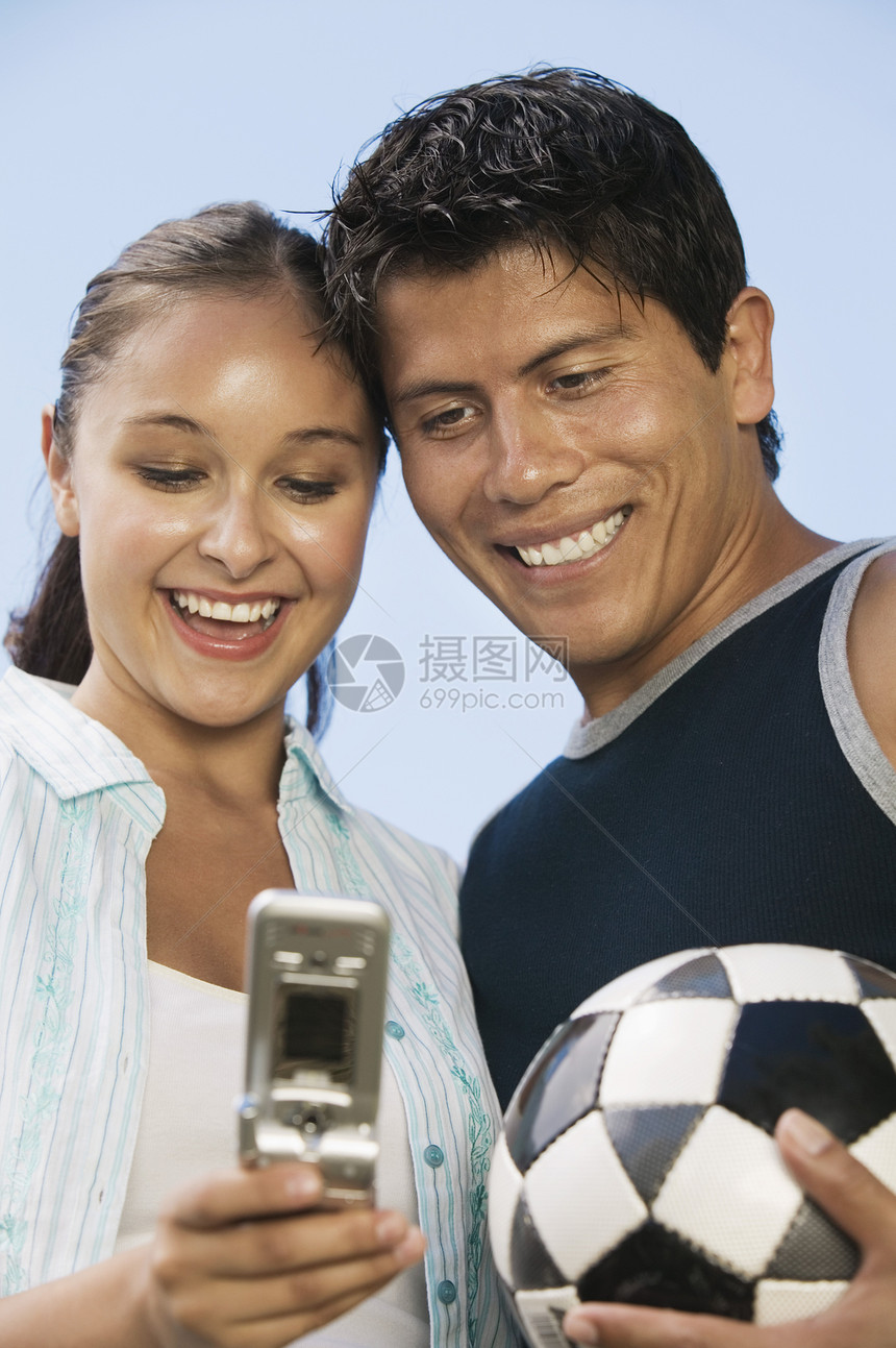 年轻夫妇使用移动电话 而男子则用足球对着晴天看球图片