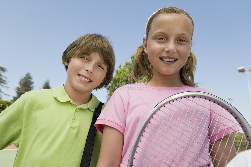 兄弟姐妹在网球场肖像特写上拿着网球拍图片