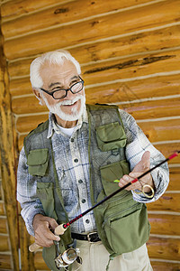 五十出头穿着捕鱼背心的西班牙裔快乐老人拿着渔棍和诱饵背景