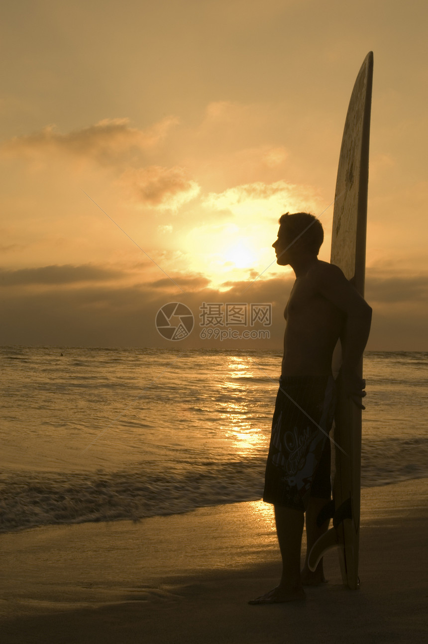 在海滩上看日落的冲浪板上的年轻人全长侧视线图片
