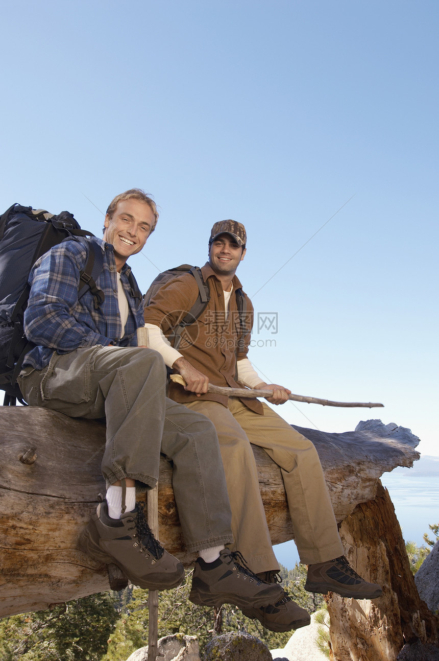 两名男性徒步旅行者坐在日志上的完整肖像图片