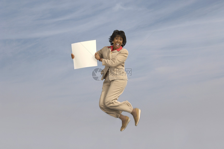 活跃的中年女商务人士在天空上用空白标志跳跃图片