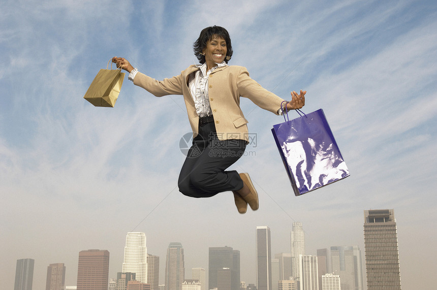一位快乐的高级女商务人士在空中用购物袋跳跃的肖像图片