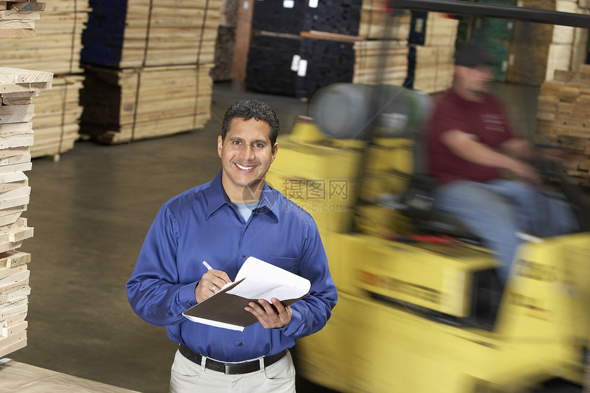 一个带着剪贴板的 微笑自信的男人的肖像 在仓库叉车前图片