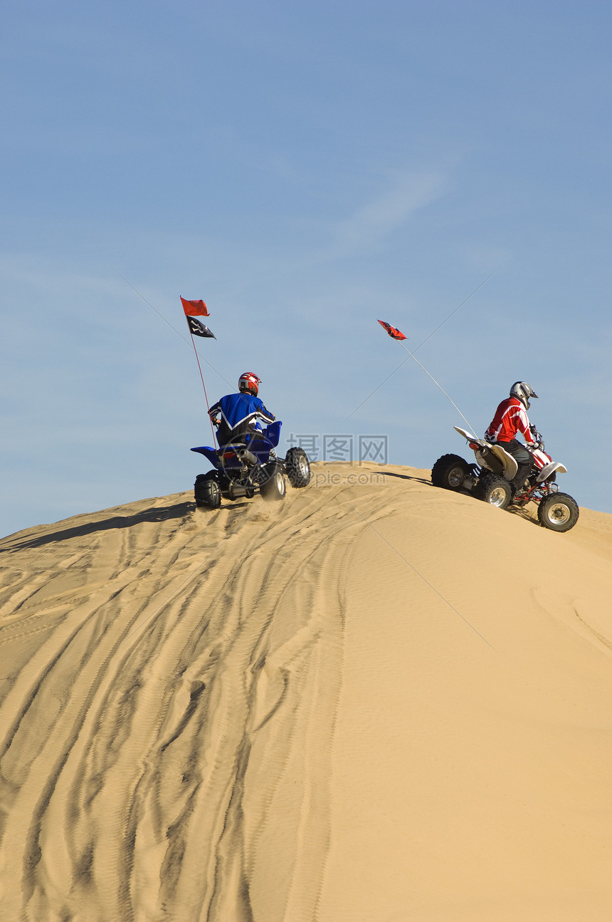 两个年轻人骑着四轮自行车 在沙漠的沙丘上图片
