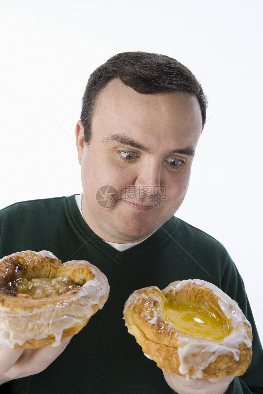 中年男子在两个美味甜甜圈之间做出抉择 两者隔绝于白种背景图片