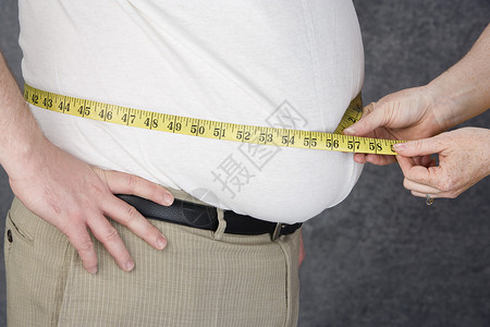 在彩色背景下测量肥胖男子腹部的手的中段高清图片