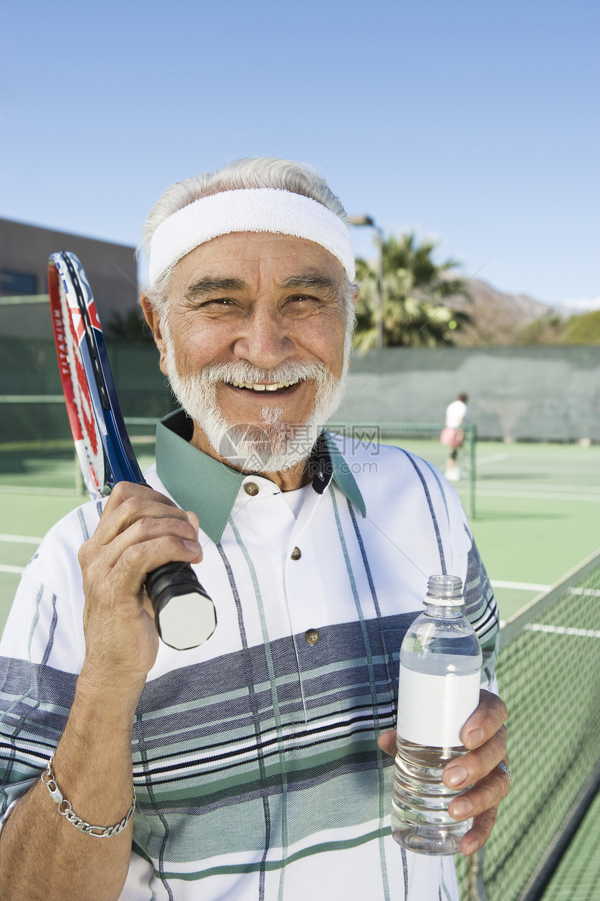 在法庭上拿着水瓶的快乐老年男网球运动员的肖像图片